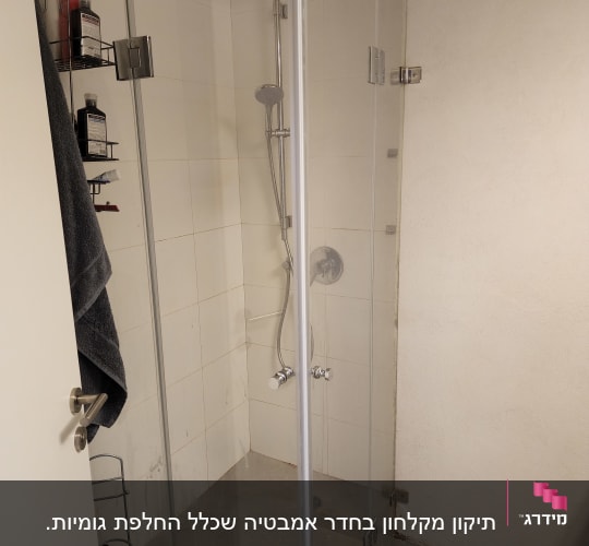 מקלחון זכוכית עם מדף בקבוקים ומגבת תלויה